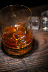 A glass of whisky with ice cubes on wooden background