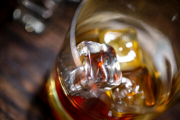 A glass of whisky with ice cubes on wooden background