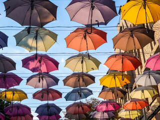 Fototapeta na wymiar colorful umbrellas decorations on city streets across blue sky on sunny day. City landscape 