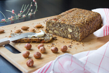 Healthy homemade keto bread with almonds, hazelnuts, sunflower seeds, chia seeds on a wooden cutting board.
