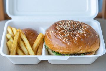 Burger with meat and French fries in paper box for delivery.