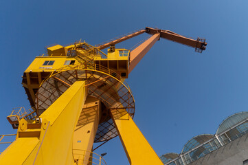 Yellow orange color crane in the sunny day with clear sky as the background. Brand new high lifter in the construction site in the background of the blue sky. Look up from the bottom on the ground.