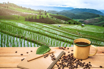 .Hot coffee cup with organic coffee beans on the wooden table over mountains landscape with sunlight and Beautiful rice fields