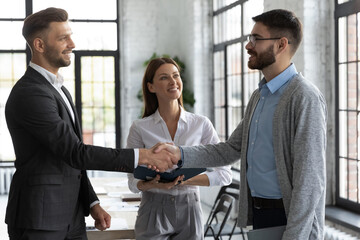 Confident business people handshaking, standing in modern office, smiling businessman shaking colleague hand, executive team leader greeting new employee, congratulating with promotion