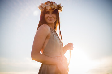 Woman in wreath of flowers and khaki dress walk in field and collect flowers. Summer sunset. Rustic style.