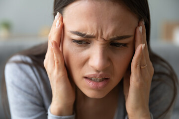 Close up view frown face of unhealthy 20s woman touches temples with hands suffers from throbbing severe headache painful feelings physical discomfort, migraine and neuralgia, emotional stress concept