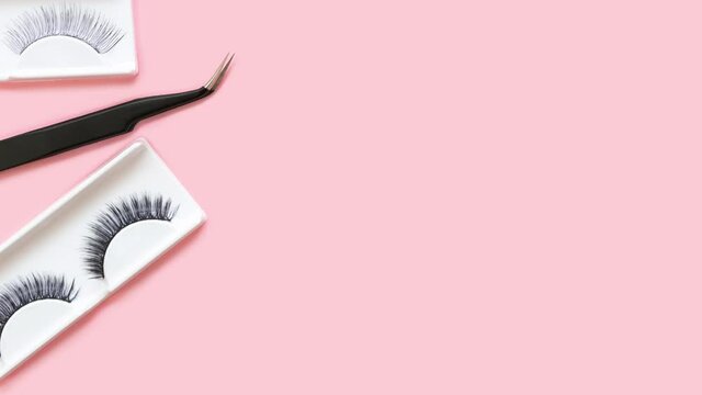 Different tools for eye lash extension on trendy pastel pink background. Fake eyelashes and tweezers. Beauty concept. Makeup cosmetics. Top view, flat lay. Place for text. Banner. Stop motion.