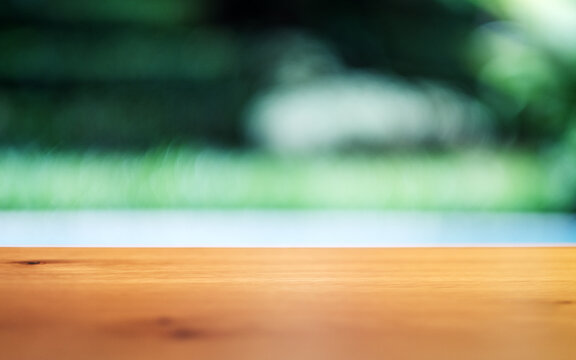 Closeup image of a wooden table with blurred swimming pool and green nature background