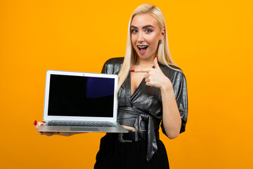 smiling young woman holding a laptop with a blank screen to insert a web page on a yellow studio background
