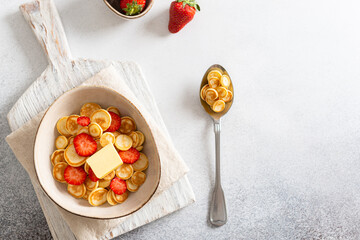 Tiny pancakes, small pancakes with butter, strawberries and honey in a bowl on white concrete background. Top view, flat lay, copy space. Menu, recipe