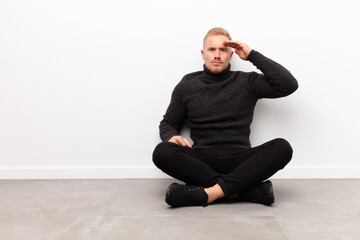 young blonde man greeting the camera with a military salute in an act of honor and patriotism, showing respect sitting on cement floor