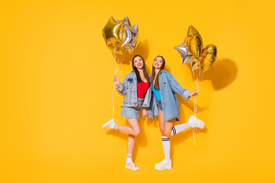 Full length body size view of nice attractive lovely slender cheerful cheery girls holding in hands air balls dancing having fun isolated on bright vivid shine vibrant yellow color background