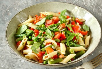 salad in a bowl of pasta, asparagus, bean pods, tomatoes, green peas, basil.