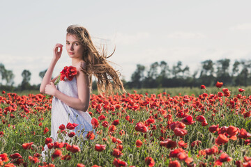 A girl in a white sundress enjoys the warmth of the sun and walks through a poppy field