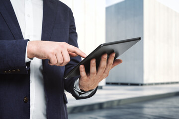 Man presses on the screen of a digital tablet near the exterior of the business center on a sunny day, close up. Online technology concept
