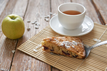 Homemade apple pie with cinnamon and cup of tea on wooden table.