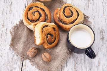 Basket of homemade buns with jam, served on old wooden table with walnuts and cup of milk