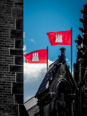 two red flags of hanseatic city of hamburg with coat of arms are waving in the wind on top of the st. nikolai memorial. horizontal photography. upright photography