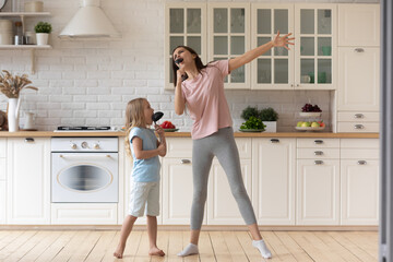 Funny young mom or nanny play sing entertain using kitchen appliances with little preschooler girl...