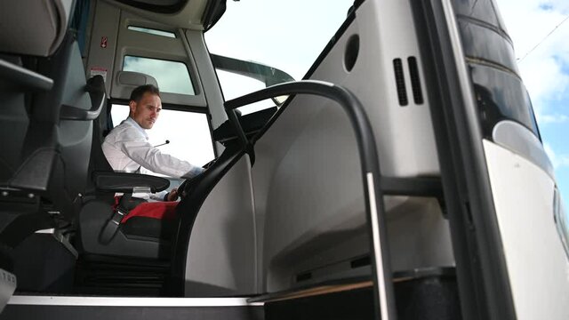 Male Coach Driver Checking Time On Wrist Watch Starting Bus And Looking Back Over His Shoulder To Check On Passengers.