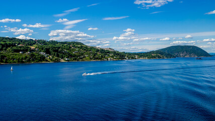 panorama of the oslofjord with two white boats in front of green hills with houses nearby saetre,...
