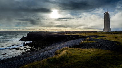 Fototapeta premium dramatic sky with a lonely unrecognizable person in the distance at malarrif lighthouse at snaefellsnes peninsula in western iceland