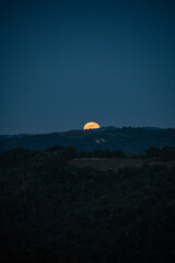 Huge super moon rising from behind the hills in a sweet spring night of may. Bright moon hovering the hills in the italian countryside. Visual poetry.