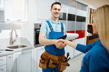 Male plumber and female customer in the kitchen - obrazy, fototapety, plakaty