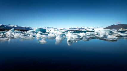 wide angle shot of ice floes floating in the cold calm water of the jökulsarlon lagoon in front of...