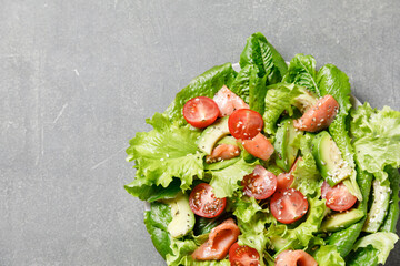 Salmon salad with avocado, green leaves, tomatoes on gray background