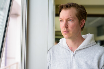 Face of young handsome man thinking and looking out the window at the gym