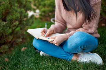 Unknown long-haired female writing in a notebook on a fresh air