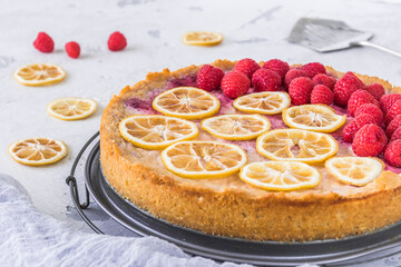 Cheese cake with raspberries and dried lemon slices on white background, some raspberries, lemon slices and cake server lying on the table. Closeup.