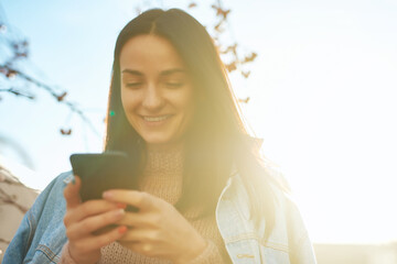 Happy lady texting by her smartphone in a beautiful sunlight