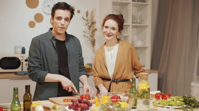 Young beautiful couple cooking dinner together at kitchen table, talking and then posing for camera and smiling