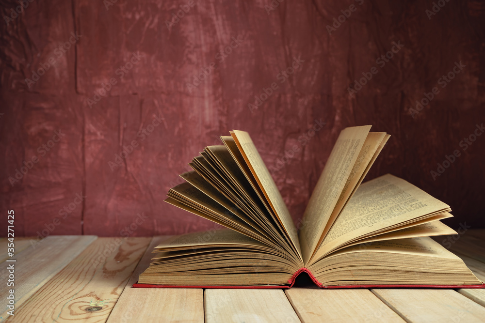 Aufkleber Beautiful ancient open old book on a red  wooden table and dark-red wall background behind.