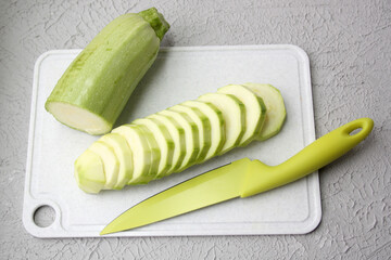Composition in one gamut. Fresh zucchini and knife lie on a plastic board. Zucchini sliced.
