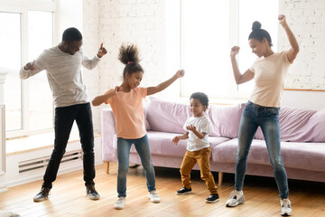 Full length view active African ethnicity couple and their kids daughter and son dancing standing in modern living room, homeowners enjoy free time together listen music spend funny activities at home