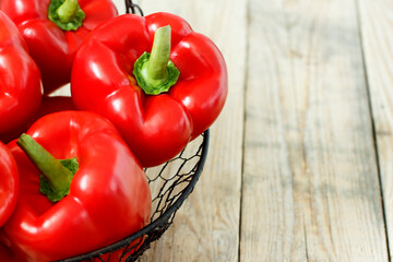 Red sweet peppers in a metal basket on rustic wooden table.