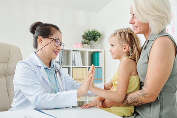 Fototapeta premium Smiling mature pediatrician giving high five to little patient after her recovery
