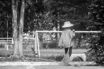 Old female cleaner and holding a sweep at the park.Black and  White style