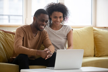 African millennial couple sitting on couch in living room make video call enjoy distant chat...