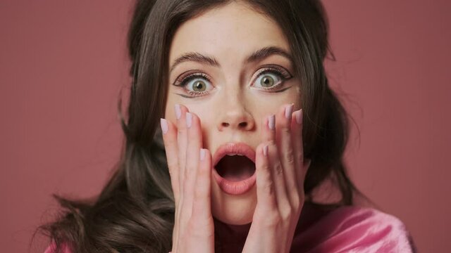 Young beautiful shocked emotional woman isolated over pink wall background