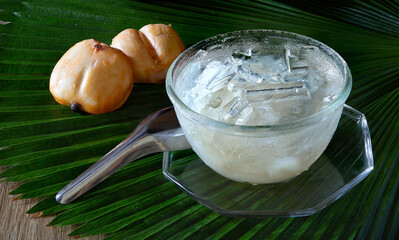 Toddy Palm fruit in syrup with ice in glass bowl put on the green plam leaf and brown wooden table