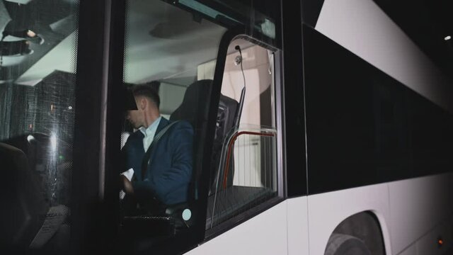 Caucasian Male Public Bus Driver At Steering Wheel Getting Ready To Start Night Shift. 