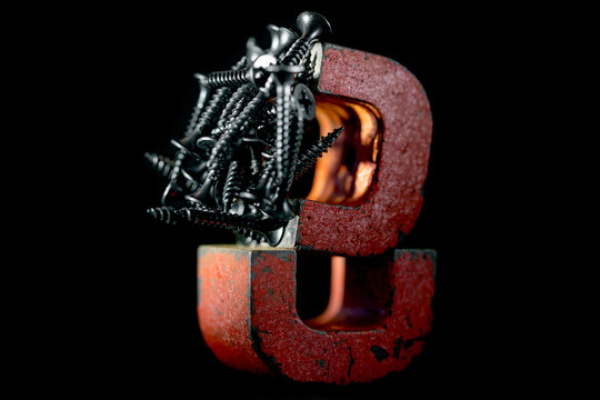A pair of red alnico horseshoe magnets with black screws on, shot against black background, low key shot