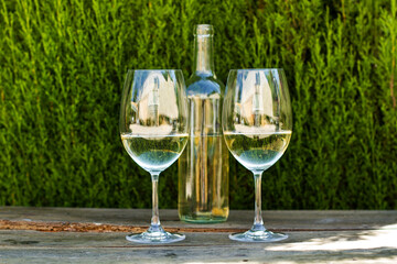 Botella de vino blanc junto a dos copas con vino con un fondo verde naturaleza sobre una emsa ústica de madera. Vista de frente