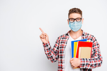 Cheerful nerd student holding book and educational materials pointing on a copyspace showing...