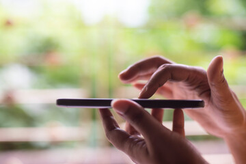 Woman operating cellphone holding with her hand in front of a window.