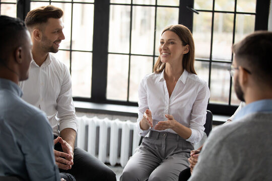 Confident Smiling Woman Coach Speaking At Meeting, Happy Diverse People Sitting In Circle At Group Therapy Session With Psychologist, Mentor Training Staff, Team Building Activity In Office